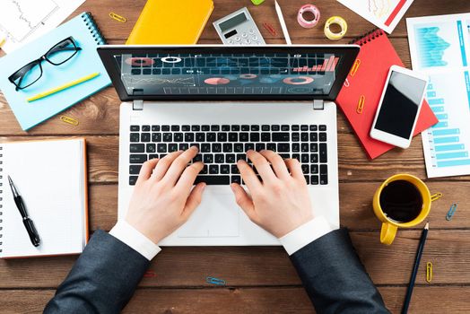 Close up business analyst working at laptop. Top view office workplace with computer and financial documents. Business occupation design with man in business suit sitting at vintage wooden desk.