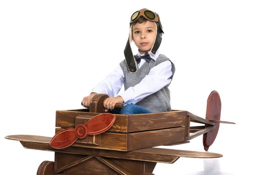 The boy in the helmet of the pilot plays with a toy wooden plane. He dreams of becoming a pilot. Concept of happy childhood, child in the family.Isolated on white background.