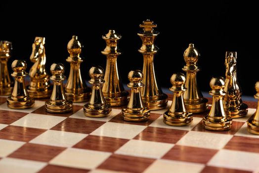 Golden chess figures standing on chessboard. Intellectual and tactic game. Strategy planning, leadership and teamwork business concept. Close-up gold chess pieces in row on black background.