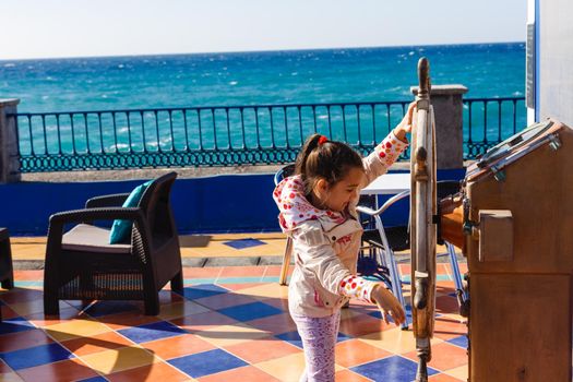 cute little girl holding a ship steering wheel in an amusement park