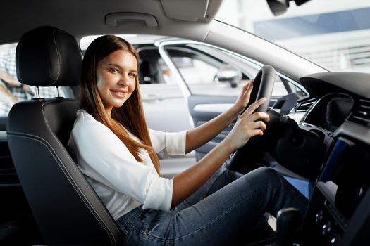 Young attractive woman looking for a new car in a car showroom
