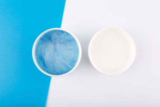 Top view of white opened jar with blue shiny face or hair mask with sea minerals against blue and white background. Concept of beauty products for face and hair moisturizing and pampering