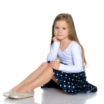 Beautiful little girl is sitting on the floor in the studio. The concept of a happy childhood, beauty and fashion. Isolated on white background.