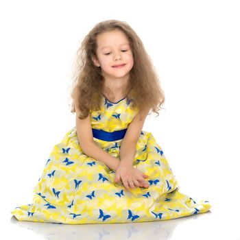 Beautiful little girl is sitting on the floor in the studio. The concept of a happy childhood, beauty and fashion. Isolated on white background.