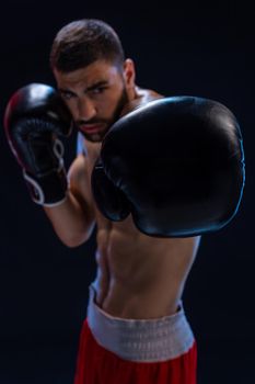 Portrait of tough male boxer posing in boxing stance against black background. Professional fighter ready for boxing match.