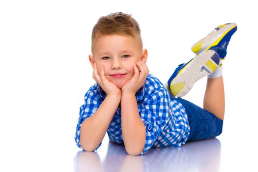 Happy little boy lies on the floor in the studio on a white background. The concept of a happy childhood, rest and vacation. Isolated.