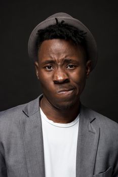 Portrait of a fashionable african american man smiling on black background. A nice guy in a gray jacket and a white T-shirt on a dark studio background. A large portrait