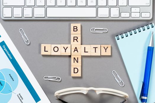 Brand loyalty concept with words from cubes. Still life of office workplace with crossword. Flat lay grey surface with computer keyboard and calculator. Strategy planning and business management.