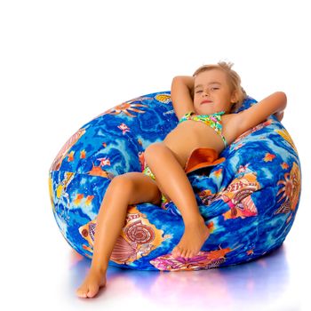 A nice little, tanned girl in a swimsuit resting on a soft pillow. The concept of summer family vacation at sea, happy childhood. Isolated on white background.