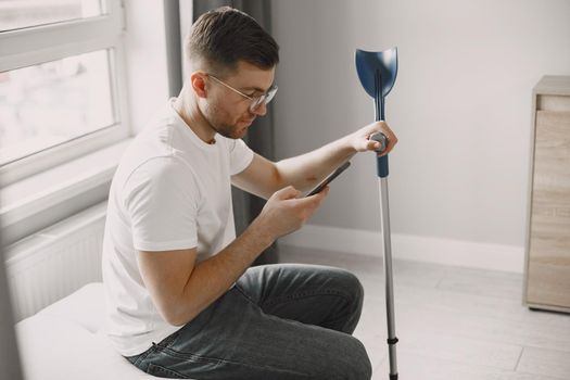 Young man with broken leg at home. Using smartphone.