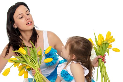 Beautiful young mother and little daughter in the same blue long skirts tutus , standing sideways to the camera ,admiring the bouquet of yellow tulips.Isolated on white background.