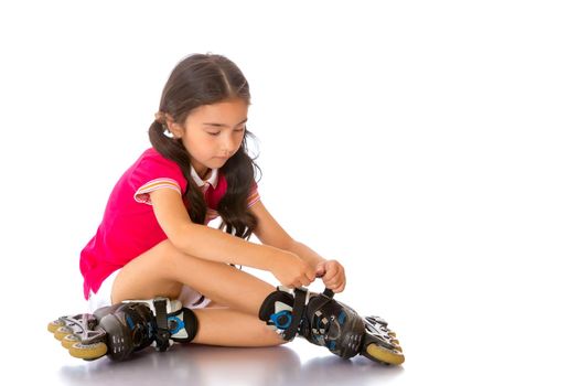 Beautiful little Asian girl puts on roller skates. The concept of advertising sports goods, a healthy lifestyle. Isolated on white background.