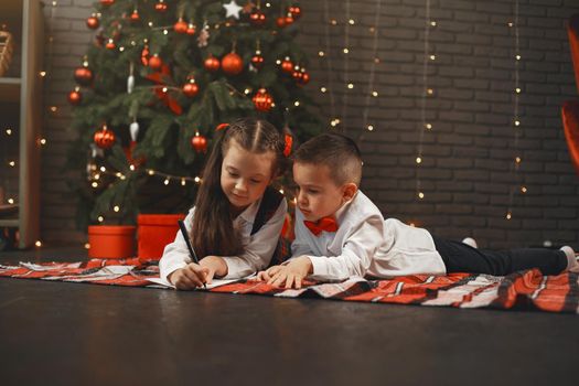 Kids sitting near Christmas tree. Children write a letter to Santa Claus.