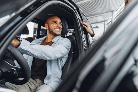 Young attractive caucasian woman salesperson in car showroom showing a car to her male African American client