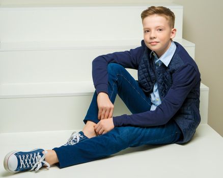 A handsome school-age boy sits on a white staircase. The concept of youth culture.