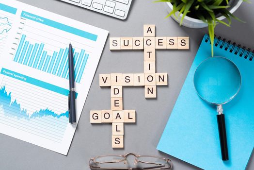 Business motivation concept with words from cubes. Still life of office workplace with crossword. Flat lay grey surface with magnifier and cup of coffee. New strategy planning and management