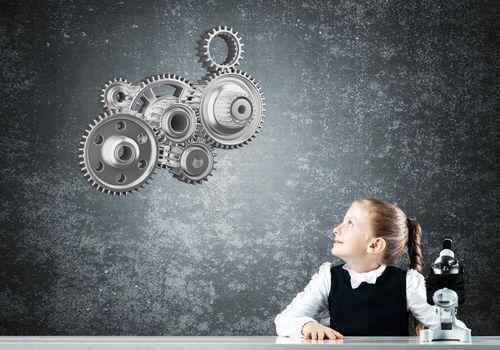 Little girl scientist with microscope on chalkboard background with gears mechanism. Research and discovery concept. Elementary science class in modern school. Schoolgirl in schoolwear sitting at desk