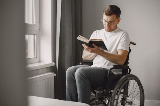 Young man handicapped. Man reading a book in wheelchair, staying at home.