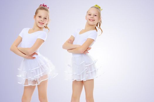 2 cheerful girls twins in white gymnastic costumes posing for the camera.On a light purple gradient background.