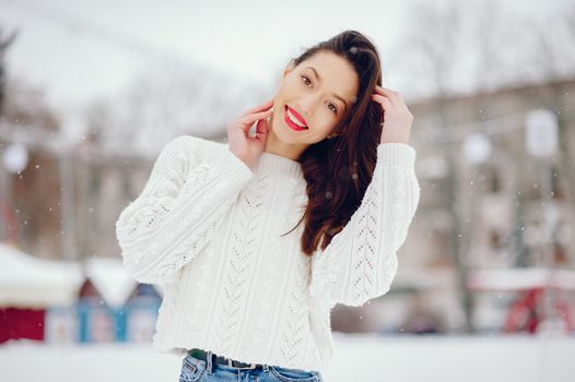 Cute girl standing in a winter city. Woman in a white sweater.