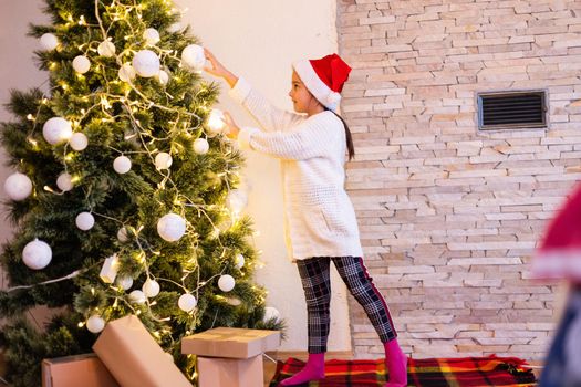 Happy kid girl laughing in room over christmas tree. Wearing stylish sweater. Childhood. Christmas time.