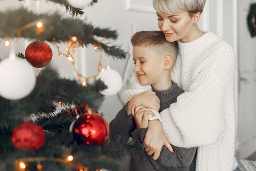 Beautiful mother in a white sweater. Family in a christmas decorations. Little boy in a room