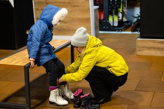 Family in a winter park. Mother with daughter in a ice arena. Mom puts her daughter in skates