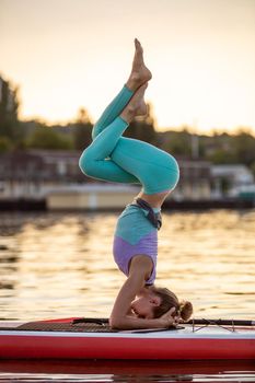 Sporty woman in yoga position on paddleboard, doing yoga on sup board, exercise for flexibility and stretching of muscles. Woman practicing yoga on the paddle board in the morning