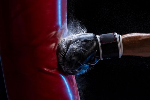 Close-up hand of boxer at the moment of impact on punching bag over black background. Strength and motivation. Studio shot