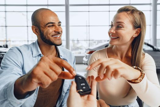 Cheerful couple taking keys of their new car in car dealership from saleswoman