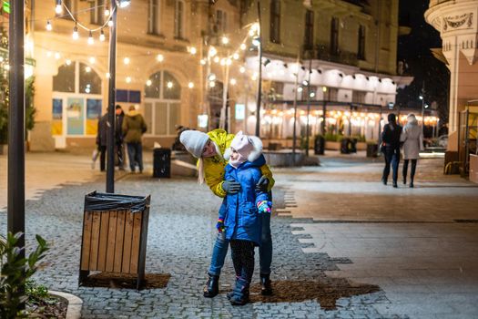 Mother with child girl at Christmas market celebrating New Year holiday. Family outdoor winter activity. Mom and daughter spend time together. Authentic lifestyle