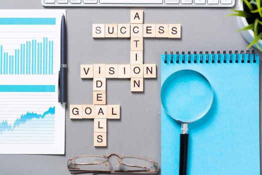 Business motivation concept with words from cubes. Still life of office workplace with crossword. Flat lay grey surface with magnifier and cup of coffee. New strategy planning and management