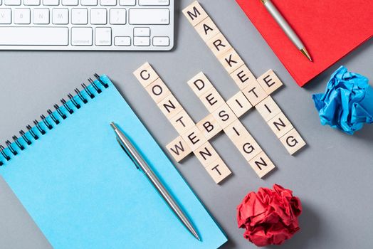 Web marketing concept with words from cubes. Still life of office workplace with crossword. Flat lay grey surface with pc keyboard and notebook. New strategy planning and workflow optimization.