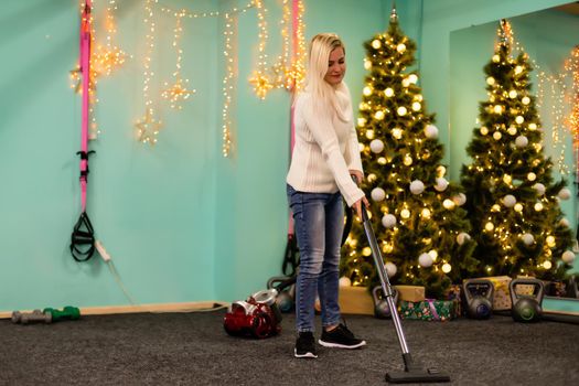 Young woman cleaning with vacuum cleaner, vacuuming under Christmas Tree needles with New Years ornaments