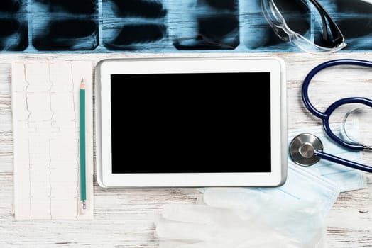 Laboratory result of patient examination lies on doctor table. Top view tablet computer with blank screen, x-ray image, stethoscope and cardiogram on wooden desk. Digital technology in cardiology.