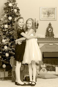 Adorable little twin girls hugging each other near the Christmas tree.Black-and-white photo. Retro style.