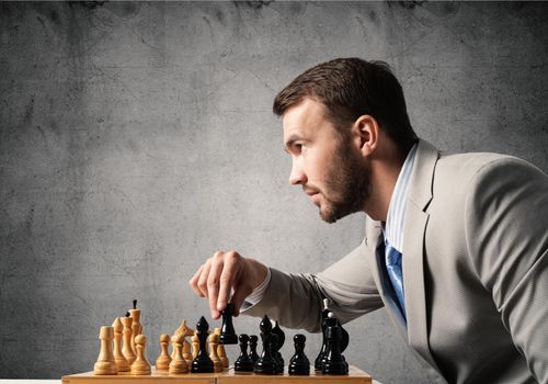Concentrated businessman playing chess game. Successful management and leadership concept. Confident young man in business suit sitting at desk with chess. Operative tactics and strategy planning