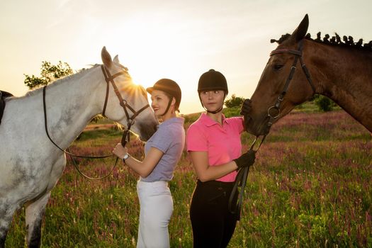 Two woman and two horses outdoor in summer happy sunset together nature. Taking care of animals, love and friendship concept.