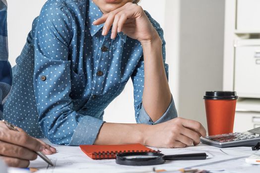 Architect standing near desk with blueprints and cup of coffee. Architecture studio concept with design project. Close up woman hand lying on technical drawing. Professional building and engineering.
