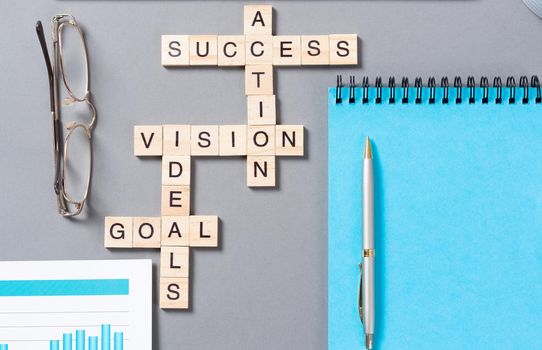 Business motivation concept with words from cubes. Still life of office workplace with crossword. Flat lay grey surface with notebook and cup of coffee. New strategy planning and management