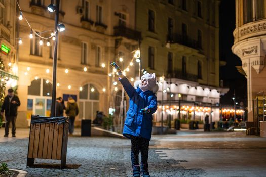 holidays, childhood and people concept - happy little girl at christmas market in winter evening.