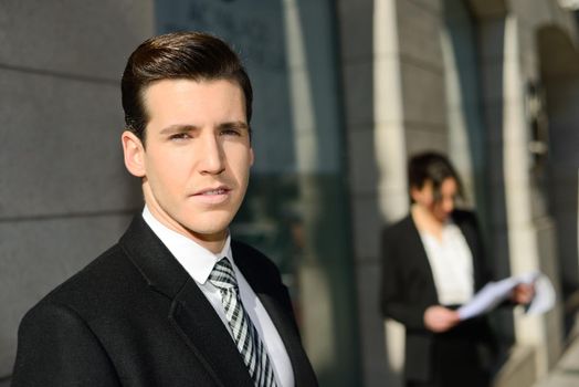 Portrait of attractive young businessman in the city with beautiful businesswoman in the background