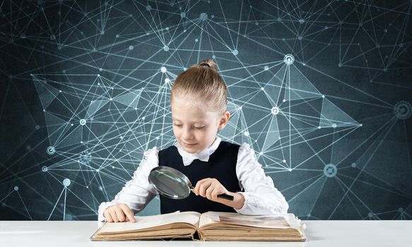 Little girl sitting at desk with magnifier and open book. Research and education in school. Happy schoolgirl in school wear carefully studying book. Clever girl reading book with magnifying glass.