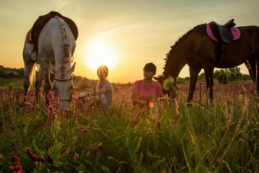 Two woman and two horses outdoor in summer happy sunset together nature. Taking care of animals, love and friendship concept.