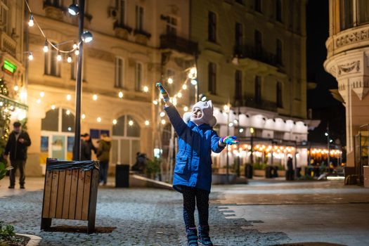 Little girl, iluminated with street lights. Christmas decoration is in the background.