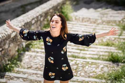 Middle-aged woman, with open arms, enjoying the sunlight in an old neighborhood of Granada in summer