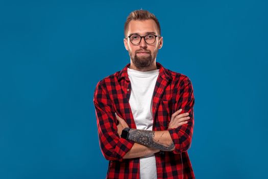 Emotional and people concept: young bearded man in checkered shirt. Hipster style. Studio shot on blue background. Copy space