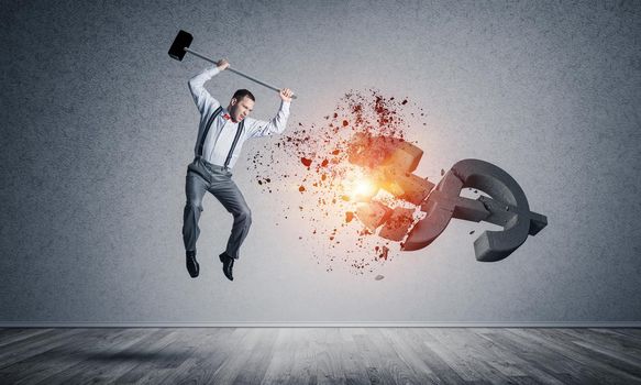 Young furious businessman crashing with hammer stone dollar symbol