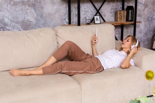 Young woman listening to music while relaxing on sofa at home. A woman is listening to music on headphones, casual style indoor shoot