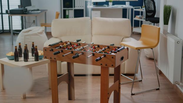 Nobody in office with foosball game table for party after work. Empty workspace with bottles of alcohol and snacks for party celebration with colleagues and businesspeople after hours.